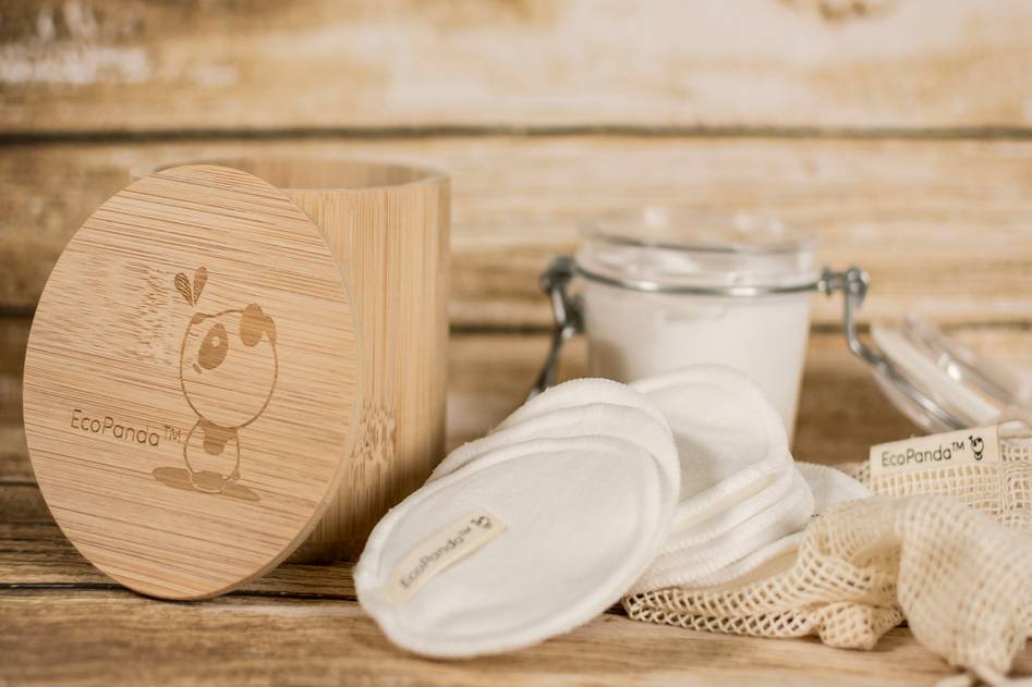 Glass jar filled with homemade organic coffee and coconut oil scrub beside fresh herbs on a wooden table